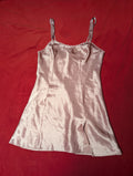 A light pink satin slip dress with thin shoulder straps and a scalloped neckline, laid flat on a red fabric background.