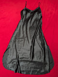 A black satin slip dress with thin spaghetti straps, laid flat on a vibrant red background.