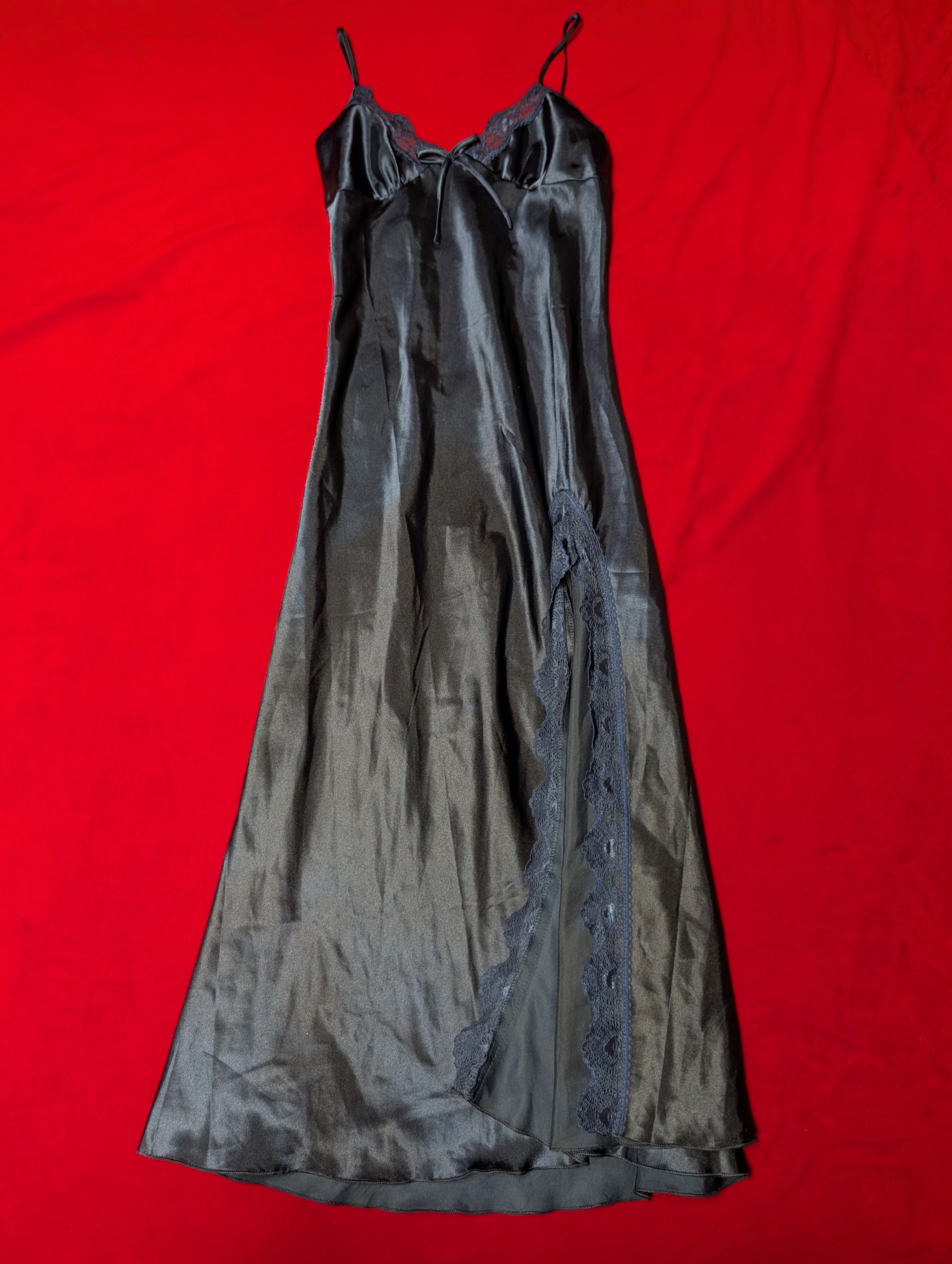 A navy blue satin slip dress with lace trim and thin straps, laid flat on a bright red background.