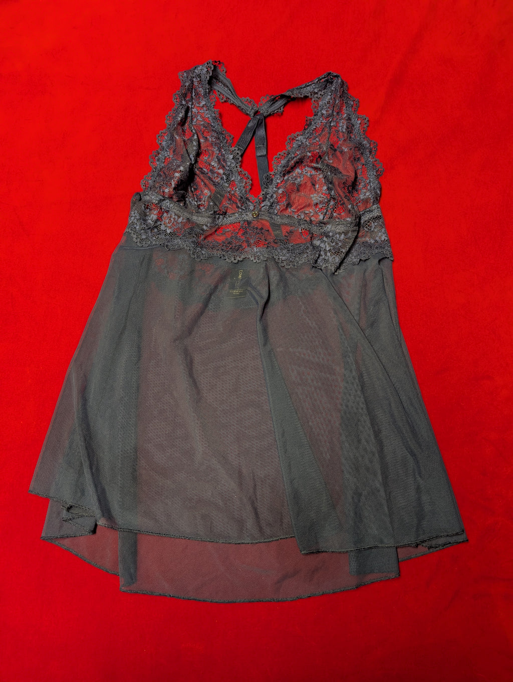A sheer navy mesh babydoll chemise with a lace halter neckline, laid flat on a vibrant red background.