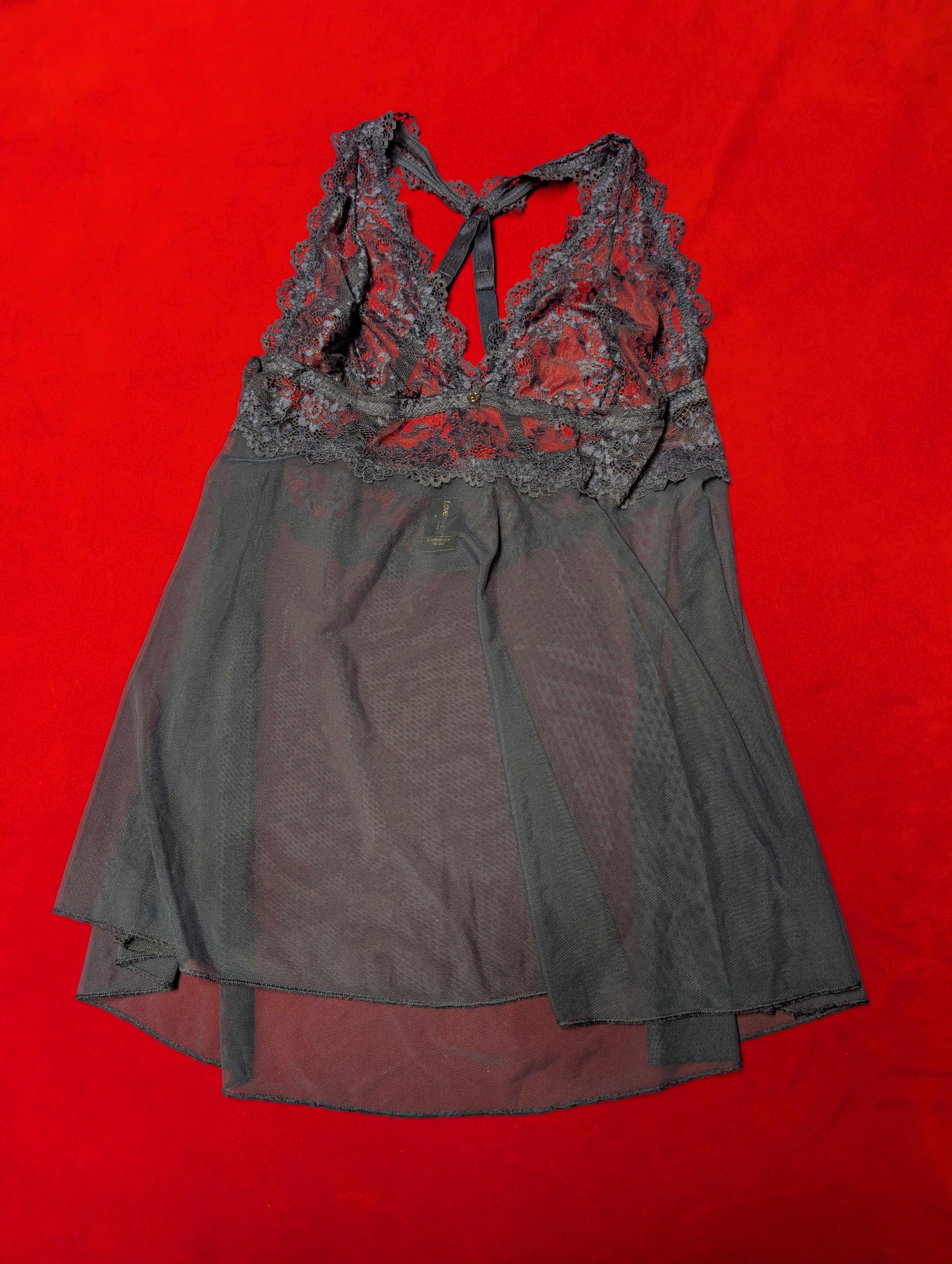 A sheer navy mesh babydoll chemise with a lace halter neckline, laid flat on a vibrant red background.
