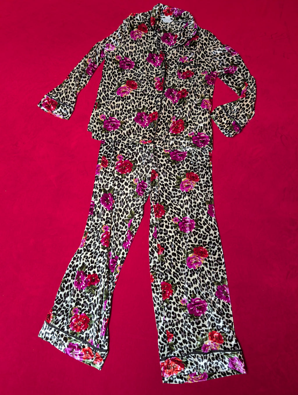 A two-piece pajama set featuring a long-sleeve button-up top and matching flared pants in a leopard print pattern with a vibrant pink and red floral print, laid flat on a bright red background.