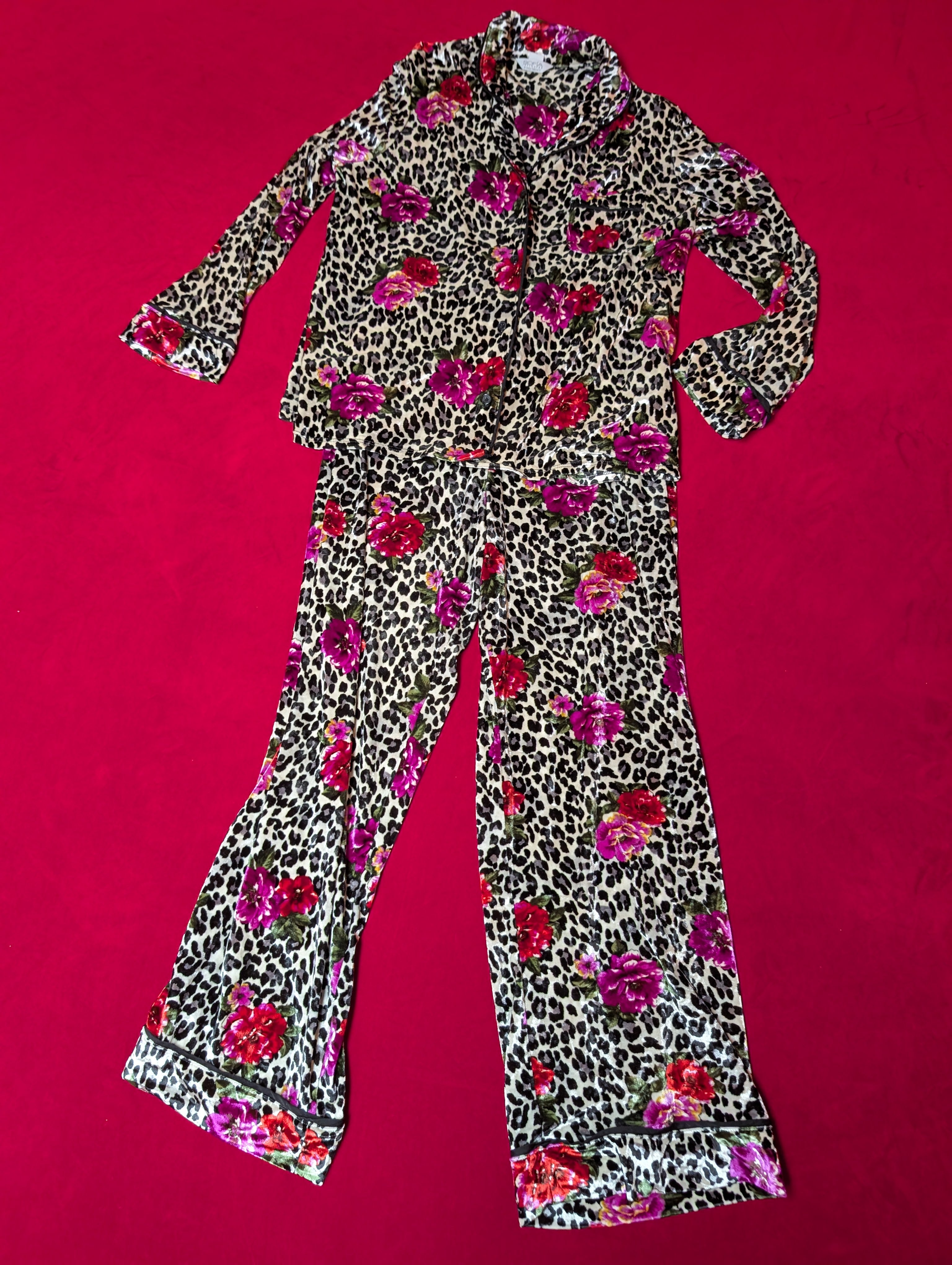 A two-piece pajama set featuring a long-sleeve button-up top and matching flared pants in a leopard print pattern with a vibrant pink and red floral print, laid flat on a bright red background.