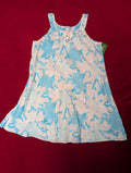 A sleeveless white tank dress with a light blue and pink tropical floral pattern, laid flat on a dark red background.