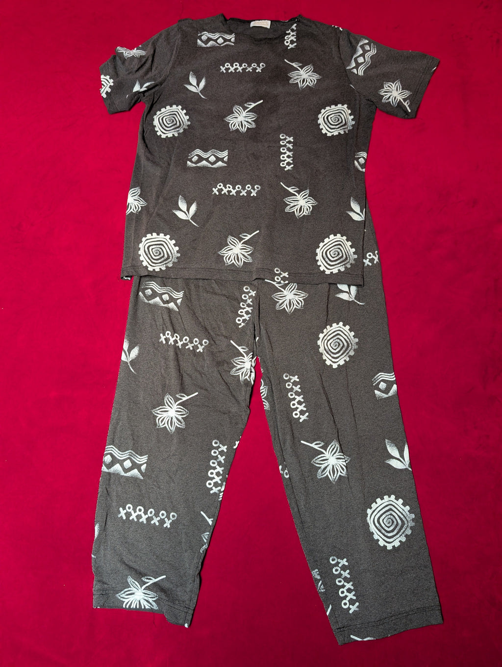 A dark gray short-sleeve pajama set with a white geometric and floral pattern, laid flat on a bright red background.