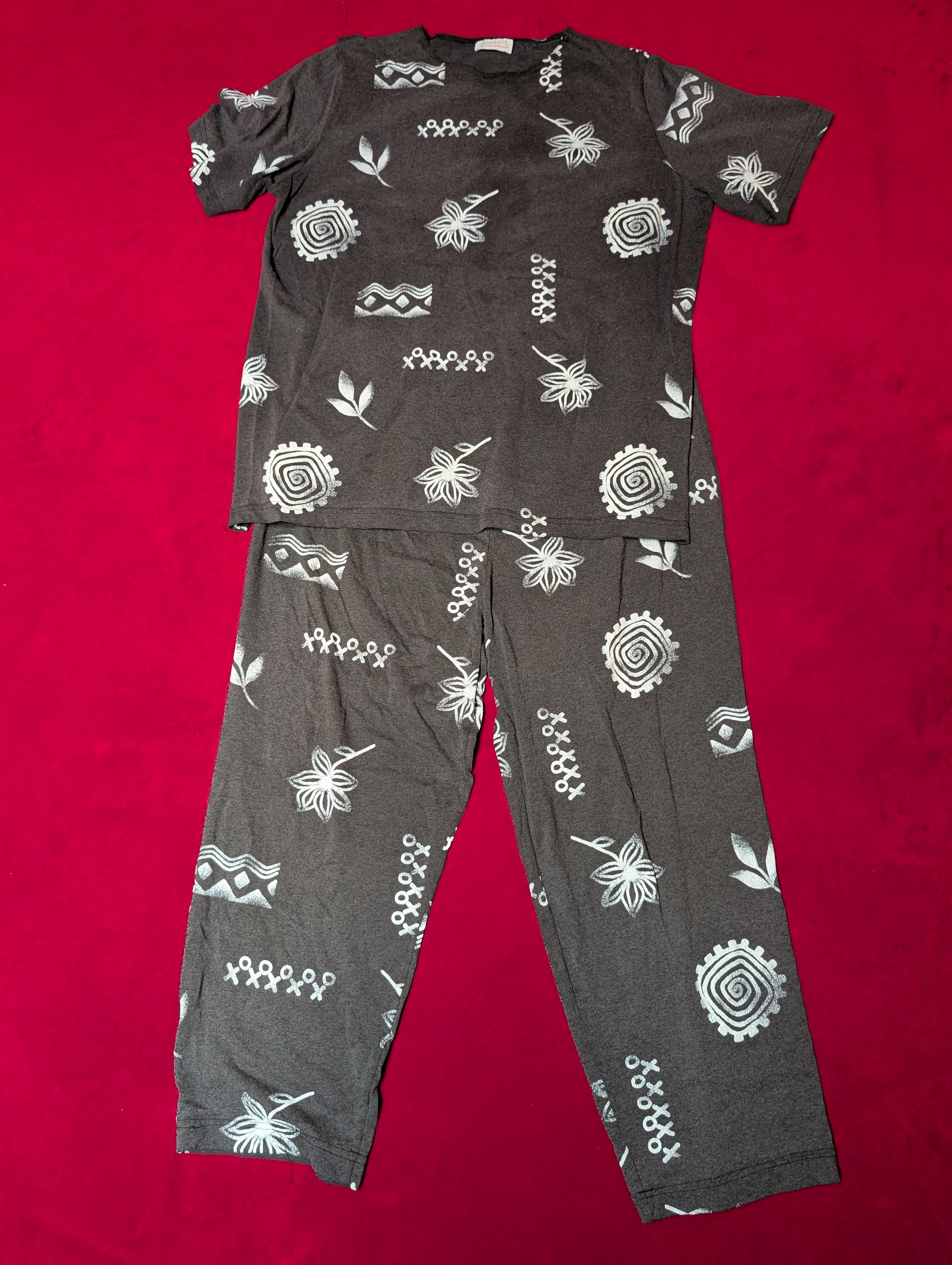 A dark gray short-sleeve pajama set with a white geometric and floral pattern, laid flat on a bright red background.