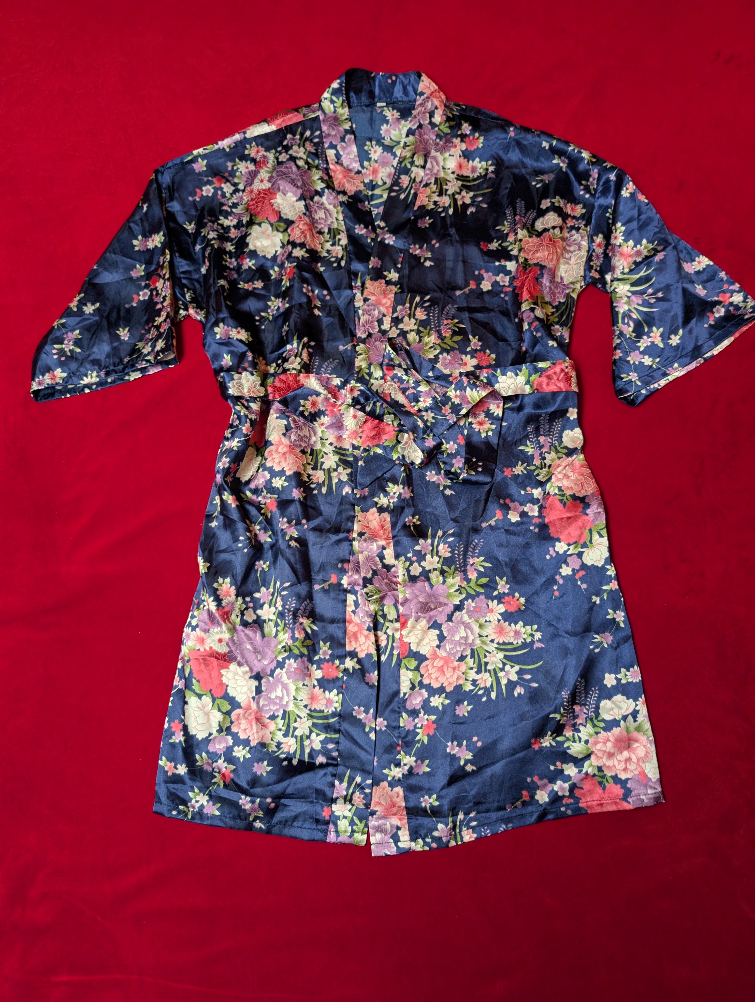A navy blue satin robe with a vibrant multicolor floral print, laid flat on a solid red background.
