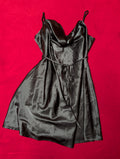 A black satin slip dress with spaghetti straps and a tie waist, laid flat on a vibrant red background.