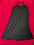A black sleeveless slip dress with thin shoulder straps and a V-neckline, laid flat on a vibrant red textured background.