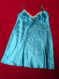 A light blue satin slip dress with thin shoulder straps and a peach-colored lace trim along the neckline, laid flat on a red background.