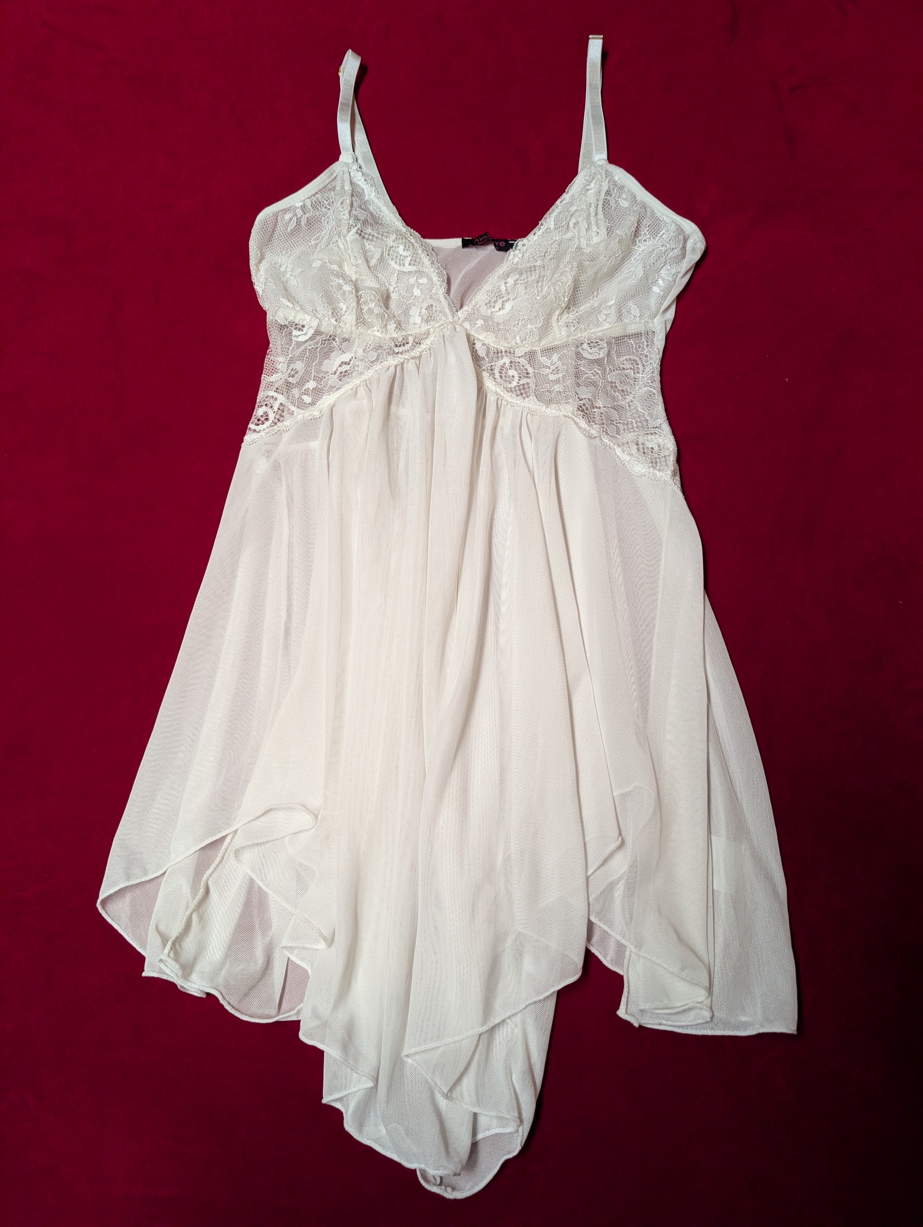 A white sheer babydoll nightgown with lace cups and thin shoulder straps, laid flat on a dark red background.