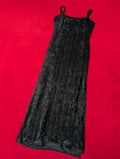 A sleeveless black textured maxi dress with thin shoulder straps, laid flat on a vibrant red background.