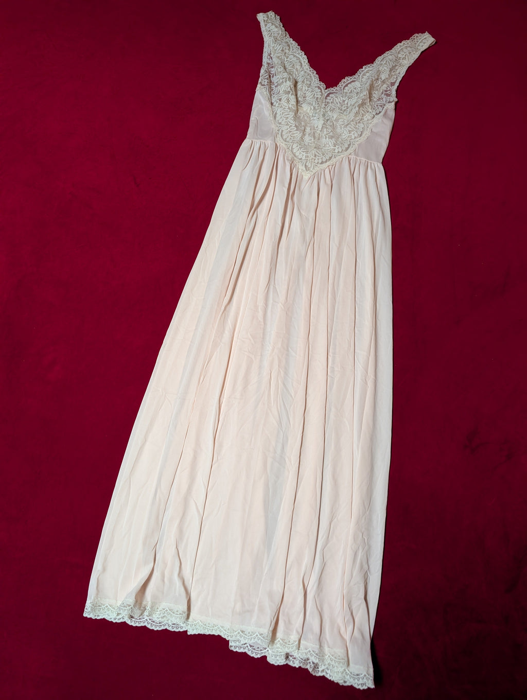A pale pink or cream-colored nightgown with a lace-trimmed scoop neckline, laid flat on a dark red background.