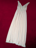 A pale pink or cream-colored nightgown with a lace-trimmed scoop neckline, laid flat on a dark red background.