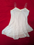 A lavender sheer babydoll lingerie chemise with thin spaghetti straps and a delicate white lace trim along the scalloped neckline, laid flat on a red fabric background.