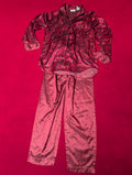 A two-piece satin pajama set consisting of a long-sleeve button-up top and matching pants, laid flat on a vibrant red background. The pajama set features a dark red and black floral pattern on the top.