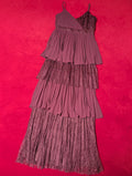 A tiered pleated dress in a deep red or plum purple color, laid flat on a vibrant hot red textured background.