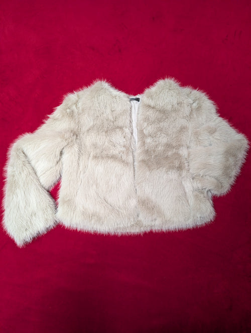 A cropped faux fur jacket in a light cream or off-white color, laid flat on a vibrant red background.