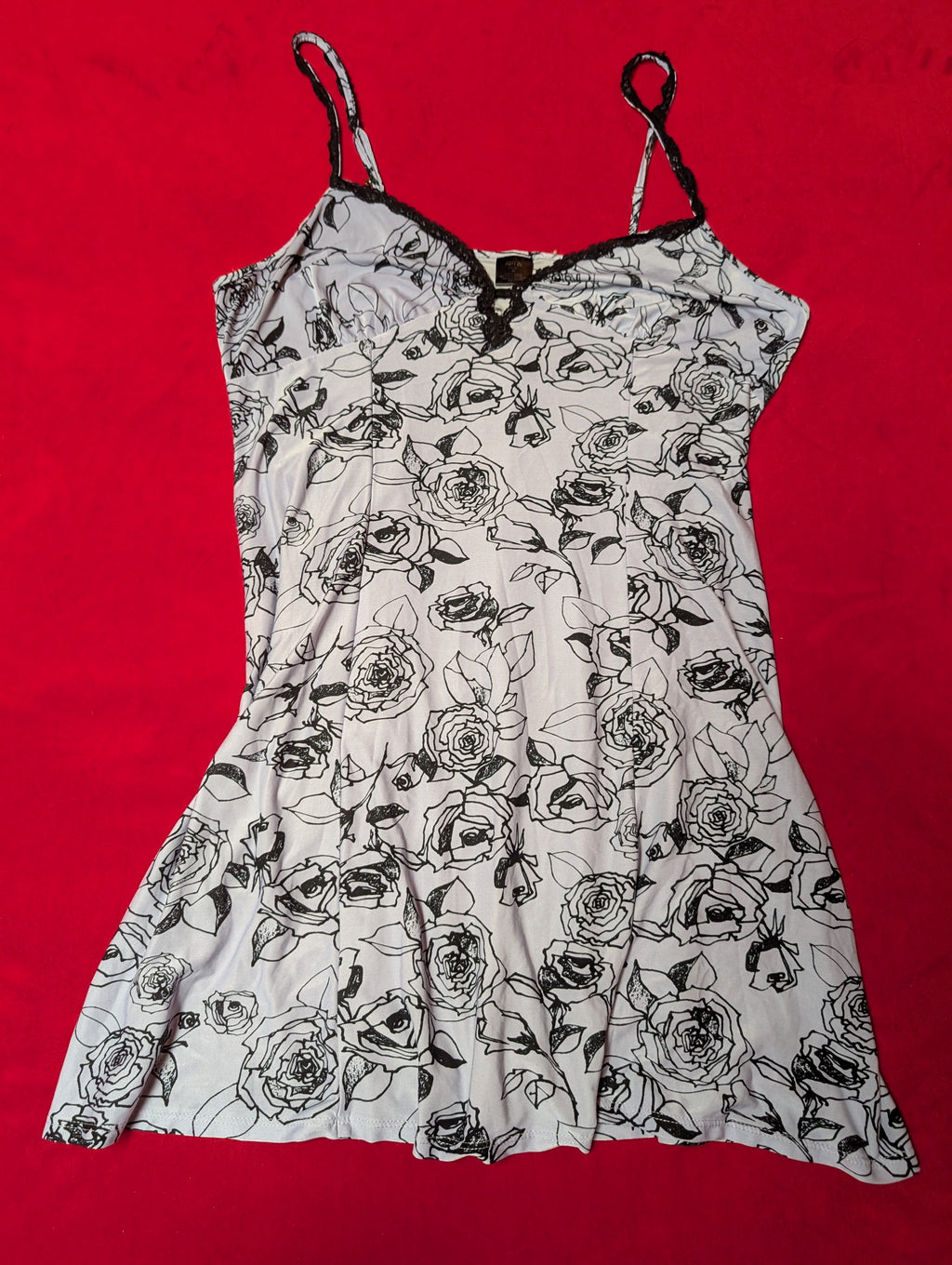 A white camisole-style top with a black rose line-art floral print, laid flat on a bright red background.