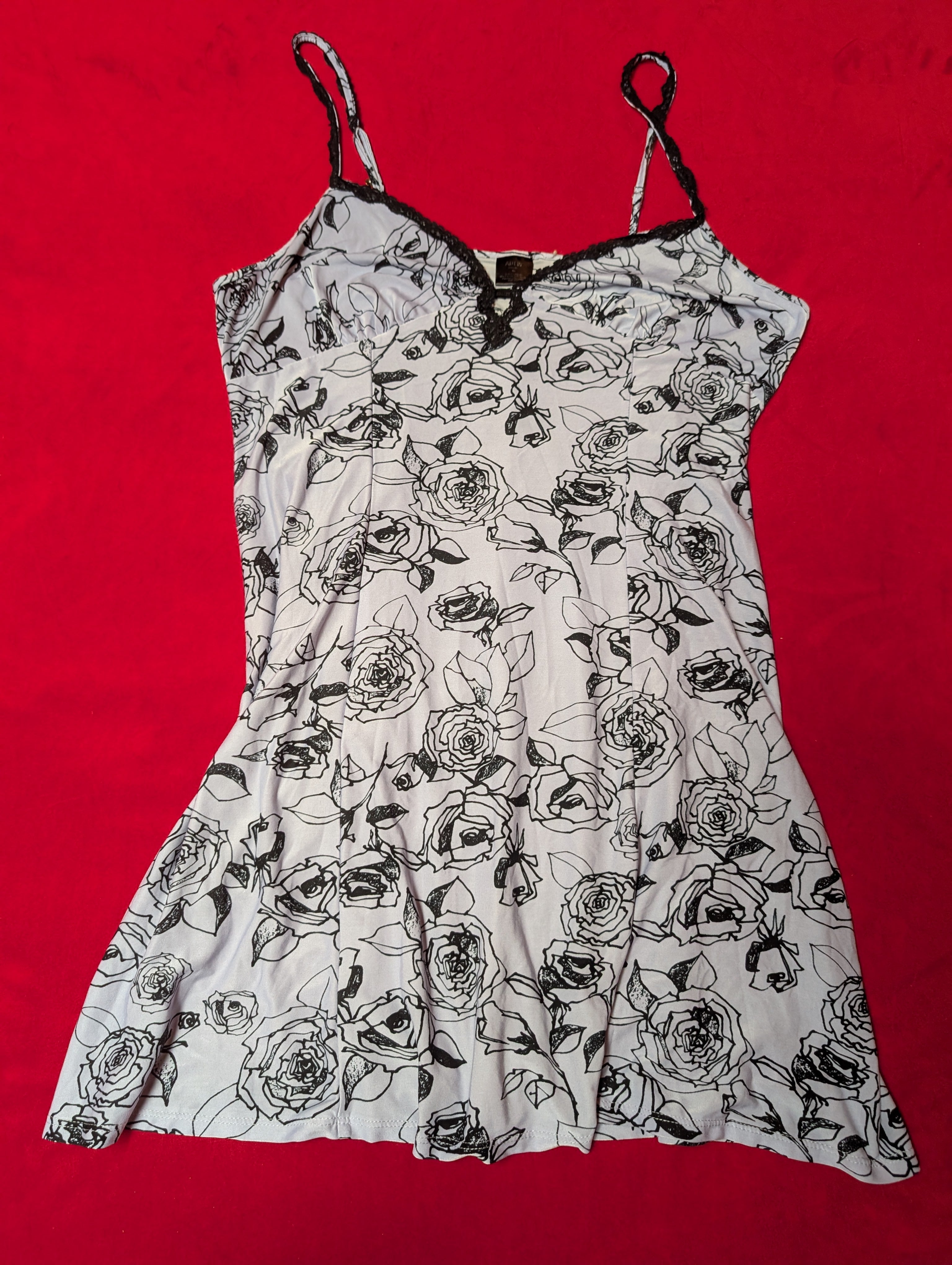 A white camisole-style top with a black rose line-art floral print, laid flat on a bright red background.