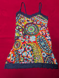 A colorful spaghetti-strap camisole dress featuring a vibrant bohemian paisley and floral print, finished with dark navy lace trim at the neckline and hem, laid flat on a red background.