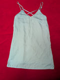 A light sky blue or pale gray-blue sleeveless camisole dress with thin adjustable spaghetti straps and a crisscross back design, laid flat on a vibrant red background.