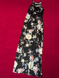A sleeveless black maxi dress with a floral print in cream, pink, and gray, laid flat on a vibrant red background.