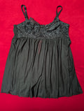 A black camisole-style nightgown with a sheer floral lace bodice and thin shoulder straps, laid flat on a bright red background.