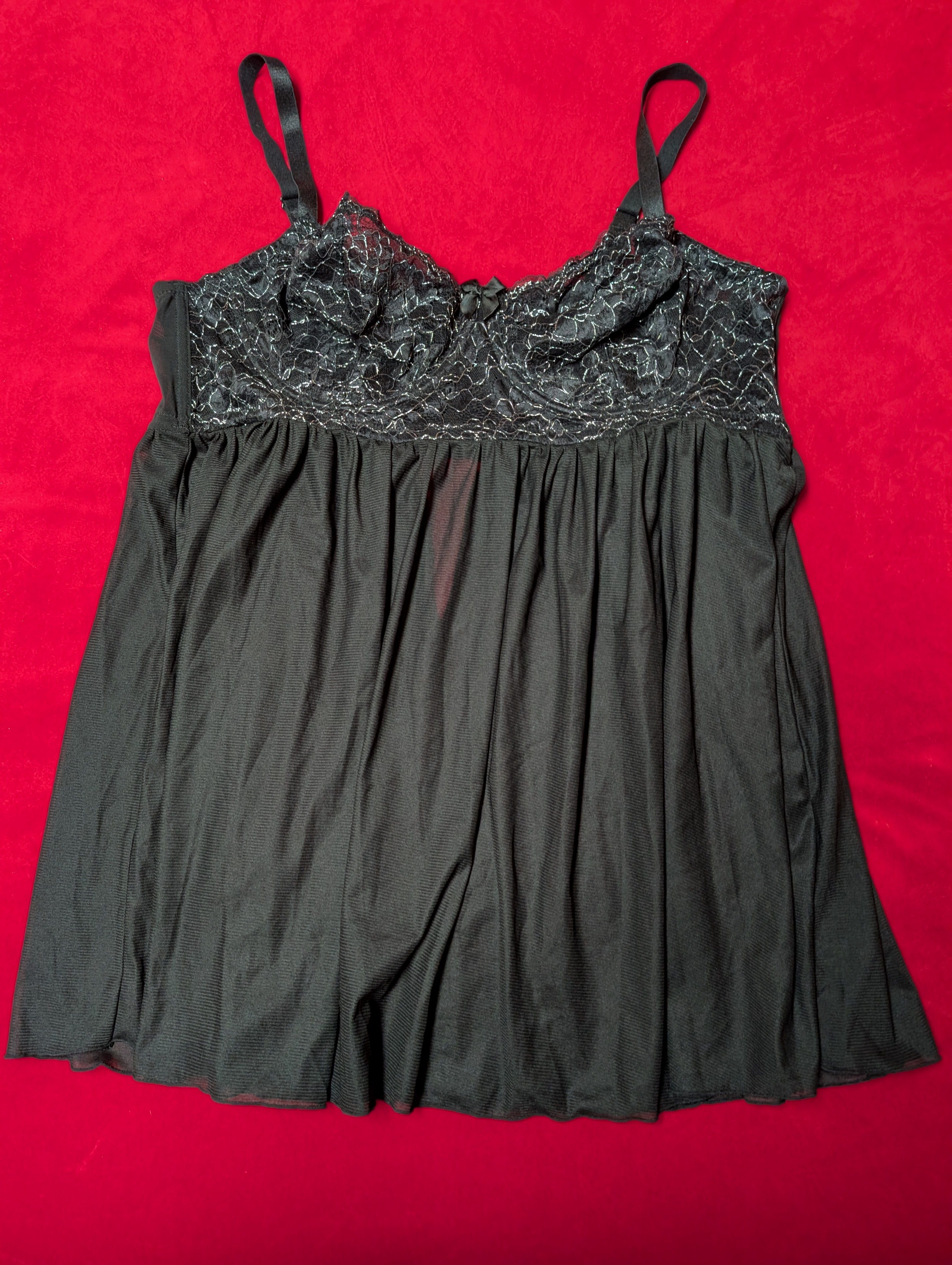 A black camisole-style nightgown with a sheer floral lace bodice and thin shoulder straps, laid flat on a bright red background.