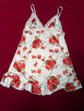 A white camisole nightgown with a red rose floral print and lace trim, laid flat on a dark red background.