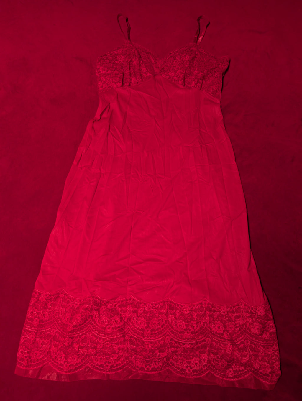 A red nylon slip dress with lace trim at the bust and hem, laid flat on a matching red background.