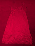 A red nylon slip dress with lace trim at the bust and hem, laid flat on a matching red background.