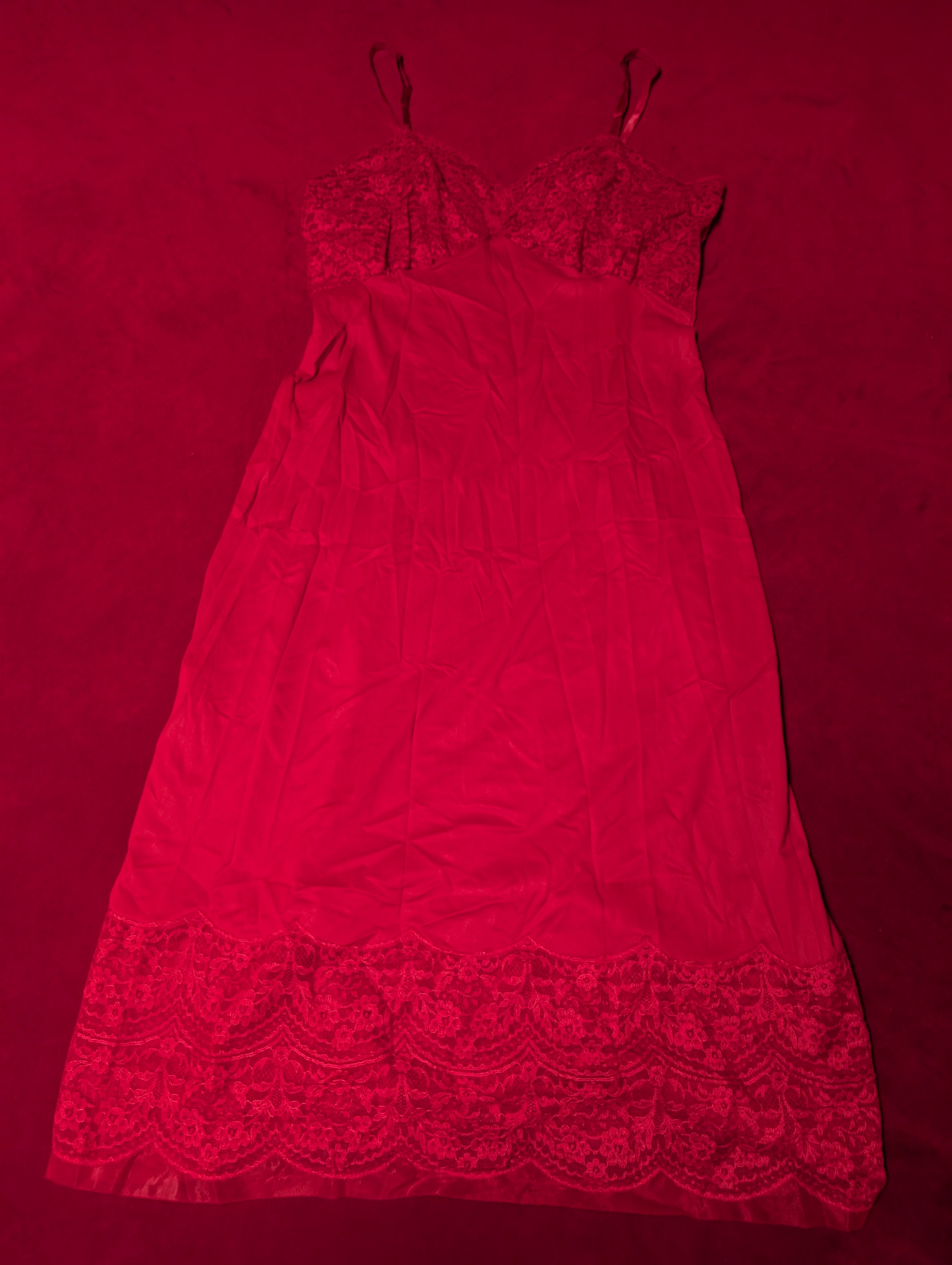 A red nylon slip dress with lace trim at the bust and hem, laid flat on a matching red background.