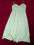 A butter-yellow colored sleeveless slip dress or long camisole with thin spaghetti straps, laid flat on a dark red background.