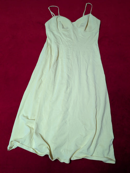 A butter-yellow colored sleeveless slip dress or long camisole with thin spaghetti straps, laid flat on a dark red background.