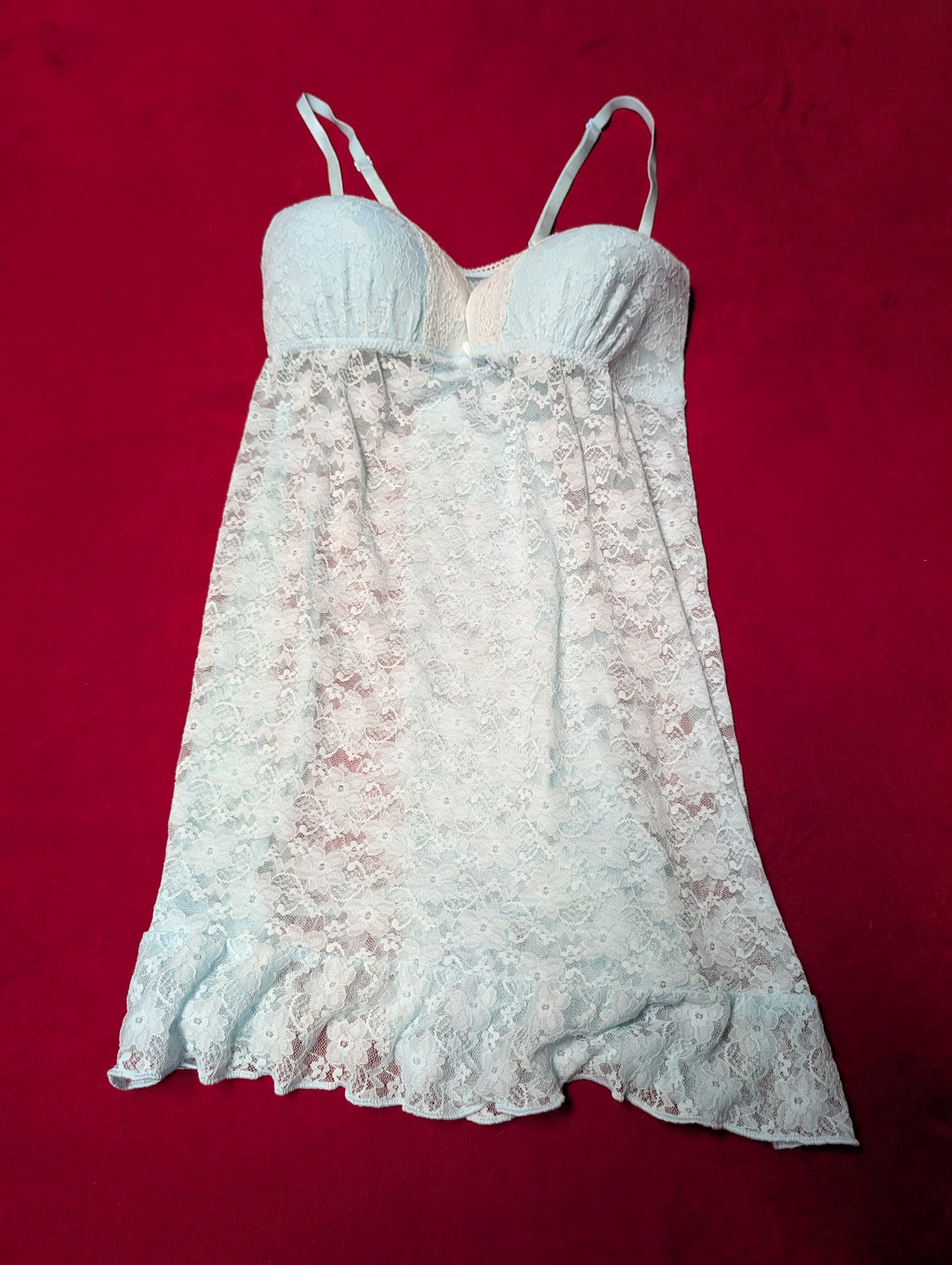 A light blue lace slip dress with thin spaghetti straps and a ruffled hem, laid flat on a solid red background.