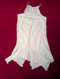A white sleeveless cotton slip or nightgown with thin shoulder straps, laid flat on a dark red background.