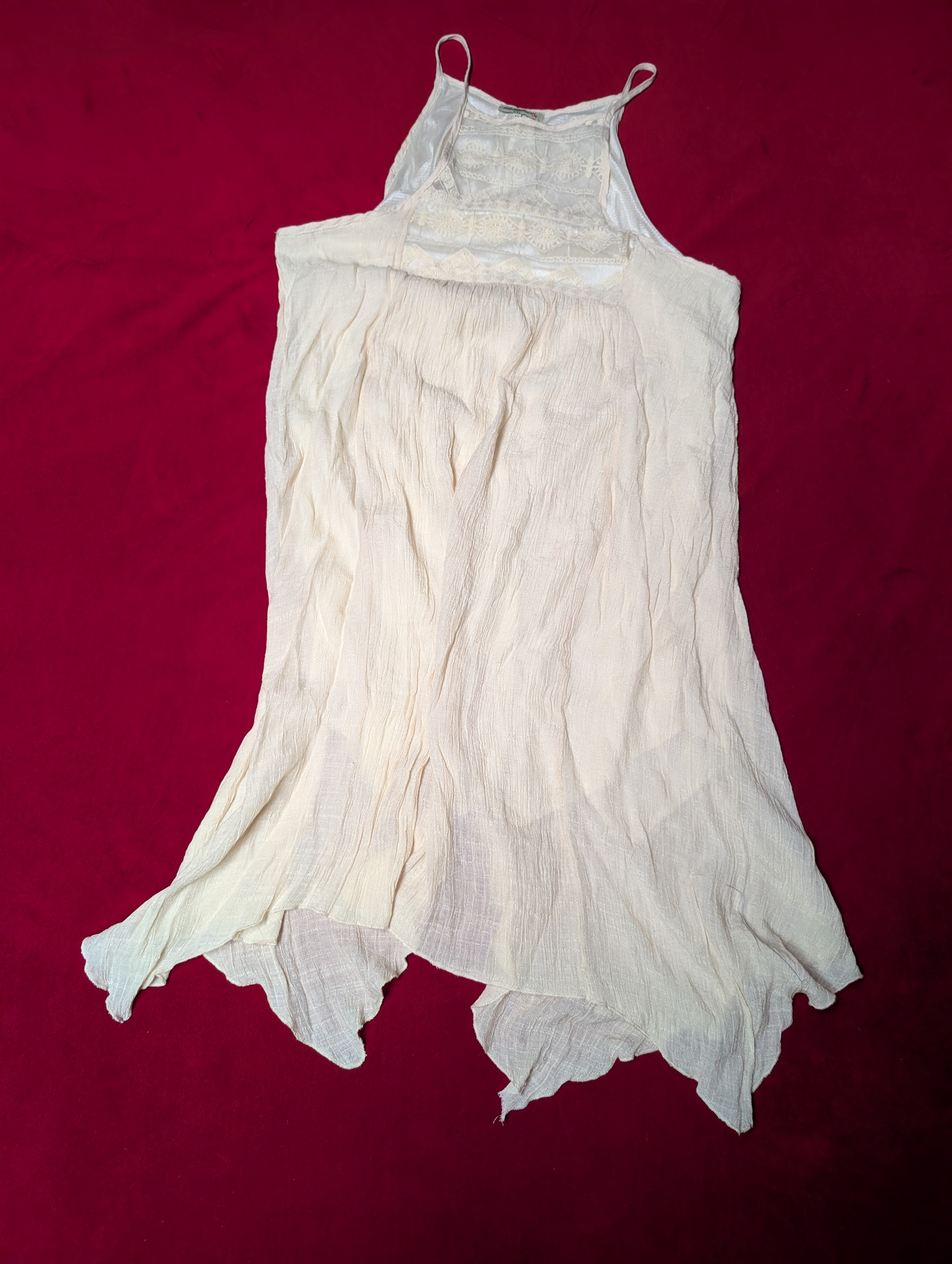 A white sleeveless cotton slip or nightgown with thin shoulder straps, laid flat on a dark red background.