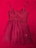 A dark red lace and tulle slip dress with thin spaghetti straps, laid flat on a vibrant red fabric background.