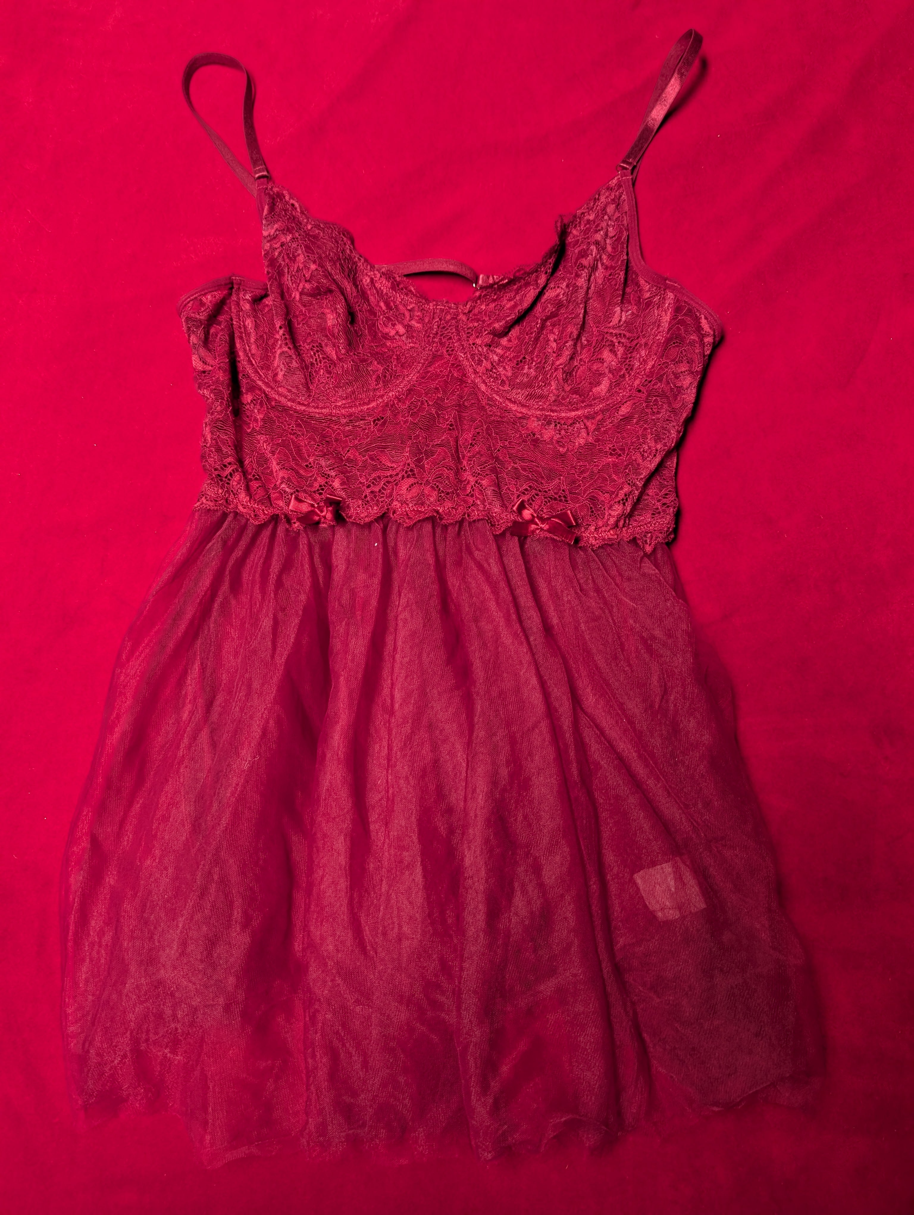 A dark red lace and tulle slip dress with thin spaghetti straps, laid flat on a vibrant red fabric background.