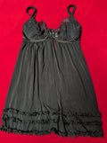 A black lace and mesh slip dress with ruffled trim, laid flat on a bright red background.