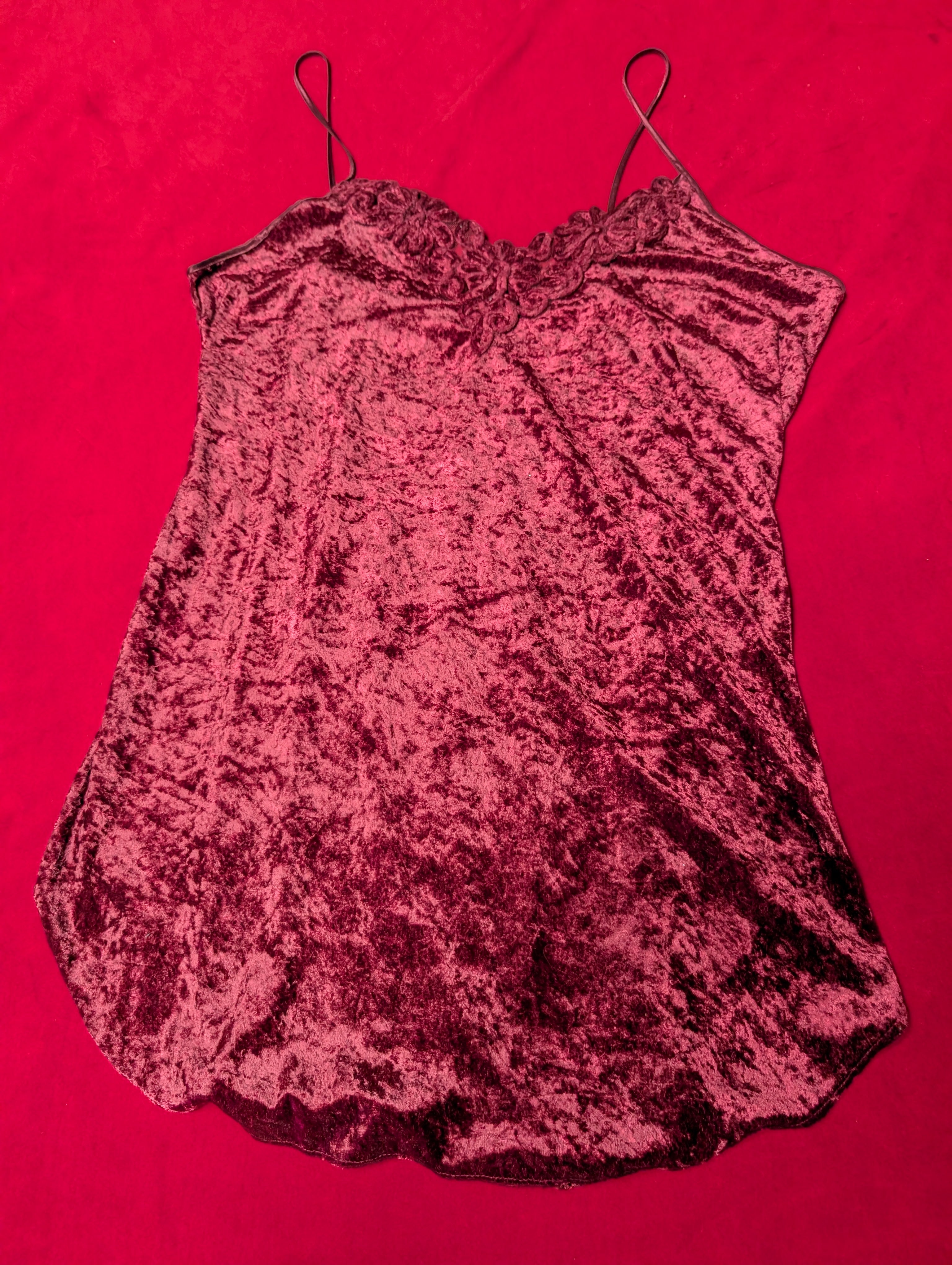 A crushed velvet camisole top in a deep burgundy red, laid flat on a vibrant red background.