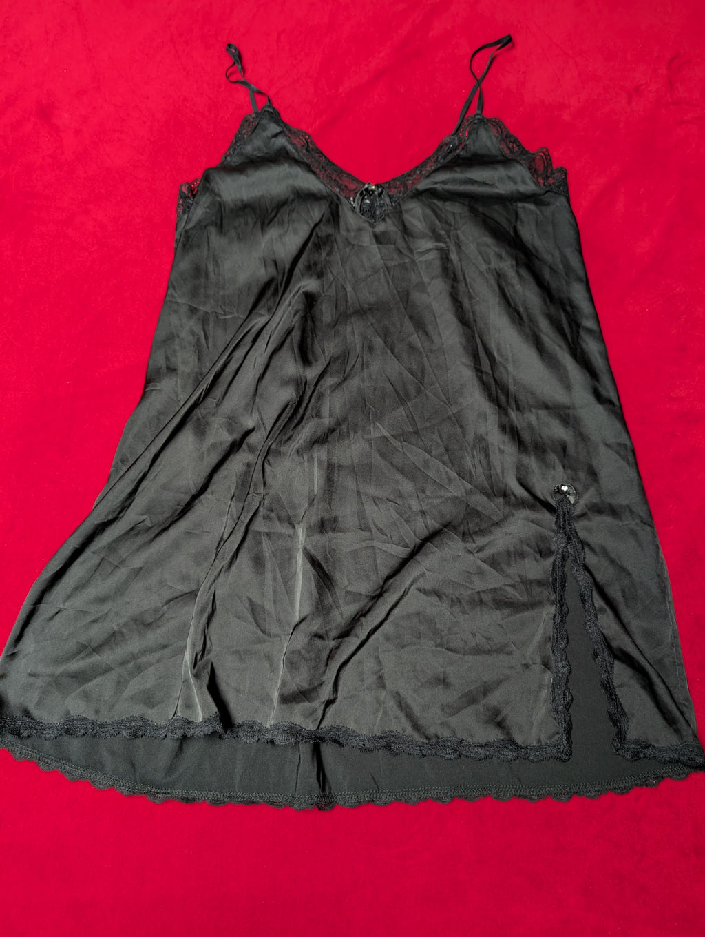 A black sheer slip dress with thin shoulder straps and delicate lace trim, laid flat on a bright red background.