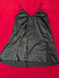 A black sheer slip dress with thin shoulder straps and delicate lace trim, laid flat on a bright red background.