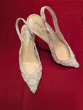 A pair of pointed-toe slingback high heels in a pale champagne or off-white satin, decorated with intricate floral lace and beadwork, displayed on a textured red fabric background.