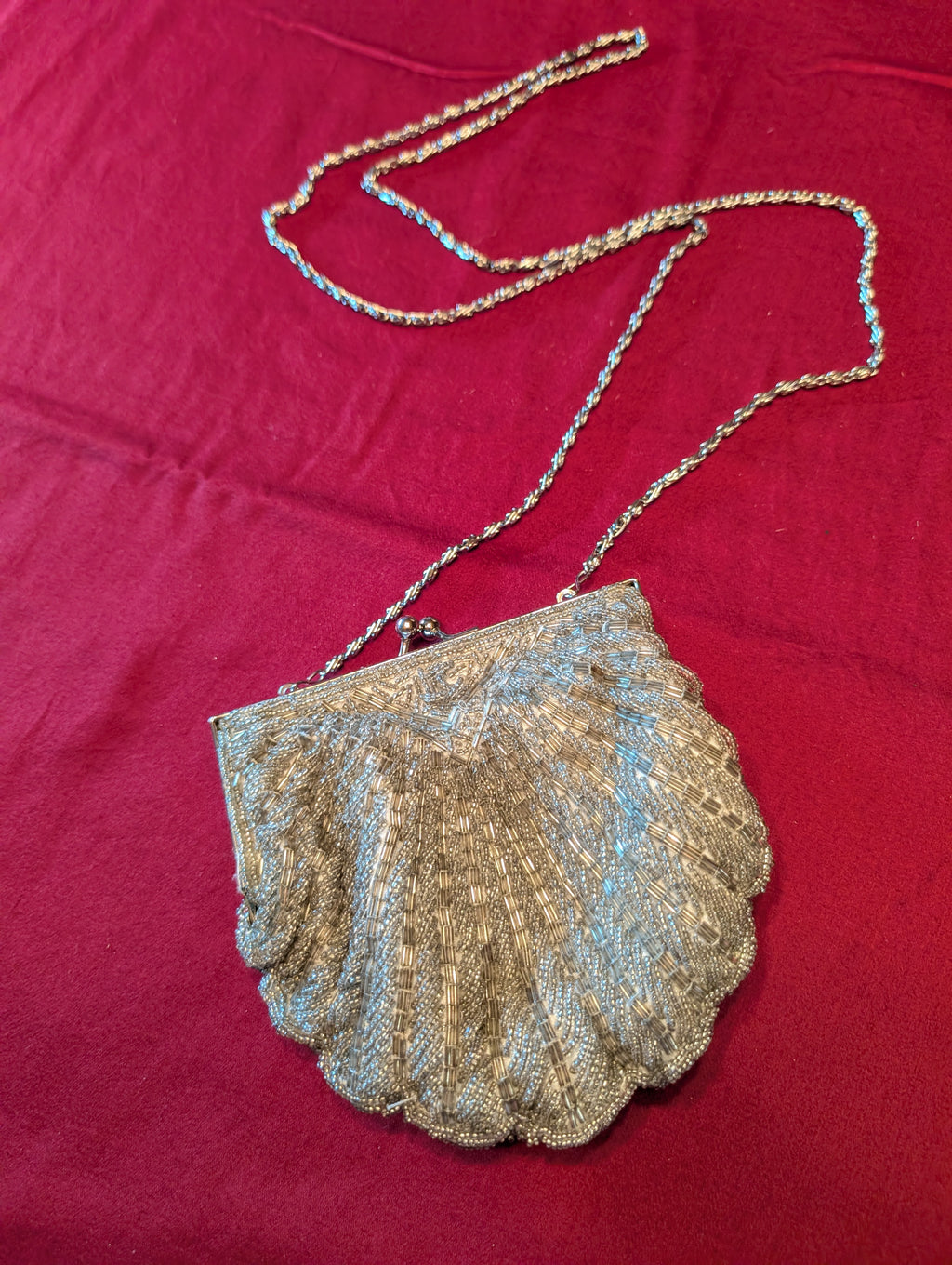 A vintage-style metallic shell-shaped clutch purse with a chain strap, laid flat on a textured magenta fabric background.