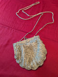 A vintage-style metallic shell-shaped clutch purse with a chain strap, laid flat on a textured magenta fabric background.